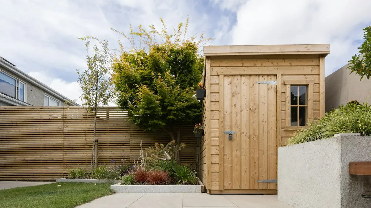 A new timber shed at the end of a pale stone patio, with a fenced lawn beside it.