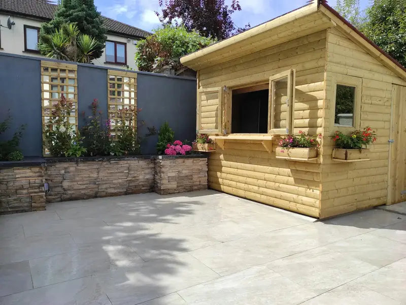 A timber summerhouse with window boxes on a pale stone patio.